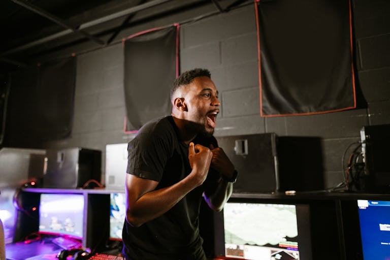 Happy gamer in a cyber café enjoying esports victory at gaming computers.