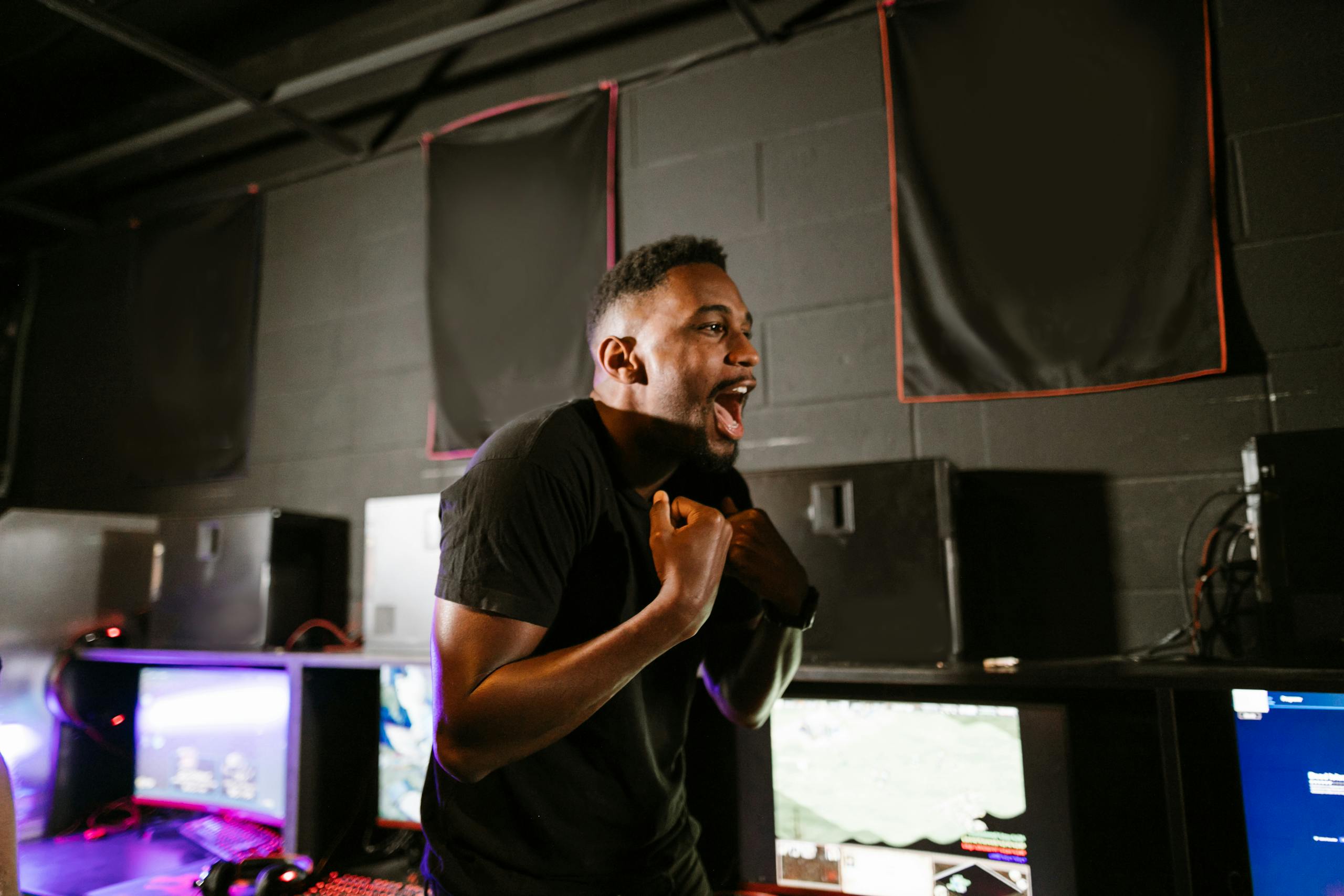 Happy gamer in a cyber café enjoying esports victory at gaming computers.